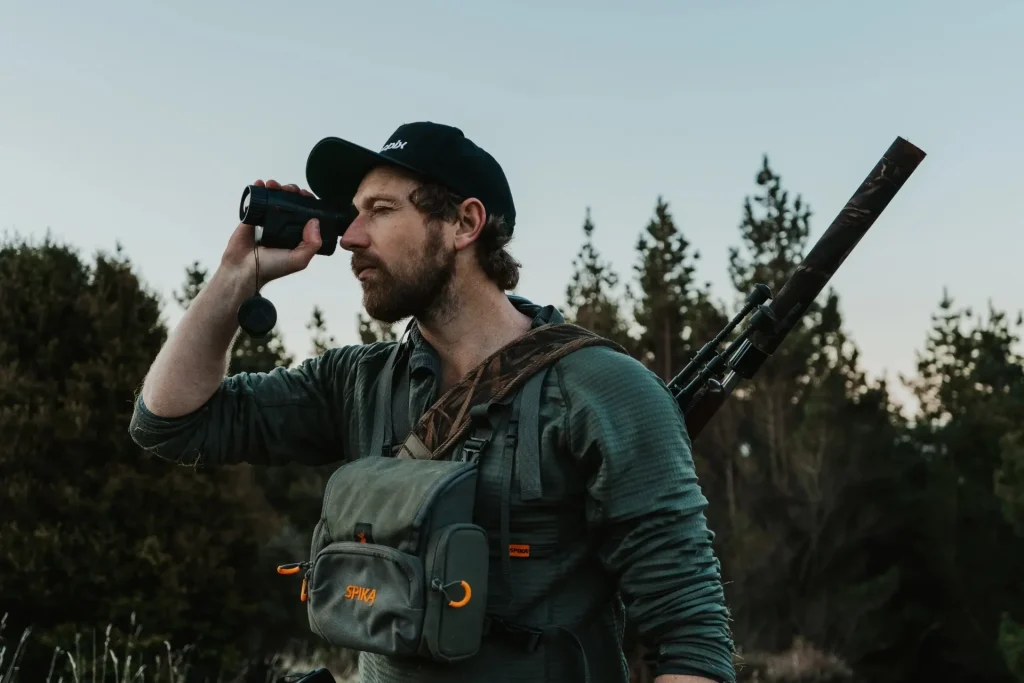 Hunter scanning a tree line with a handheld thermal monocular for hunting