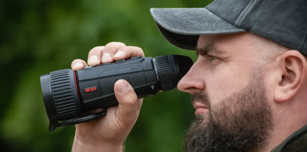 Bearded man looking through Nocpix VISTA handheld thermal imaging device outdoors.