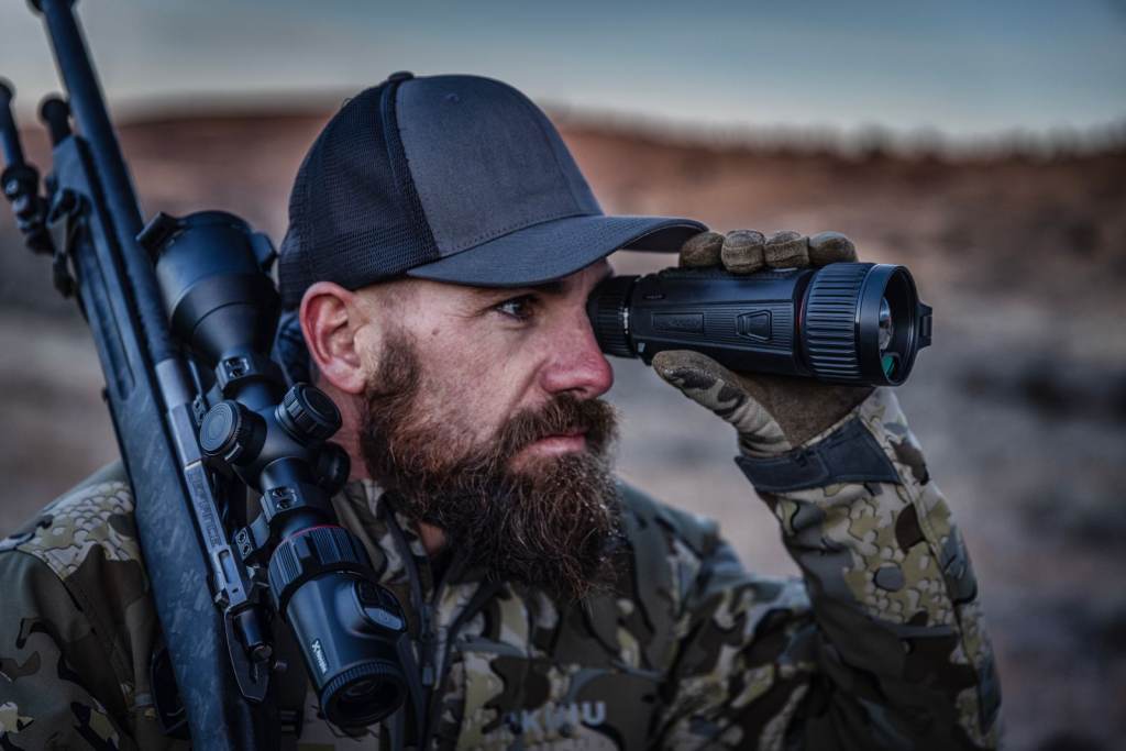 Jägare som håller ett gevär och tittar genom en handhållen monokikare utomhus.