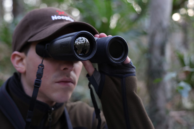 Primer plano de un cazador utilizando binoculares en un bosque.