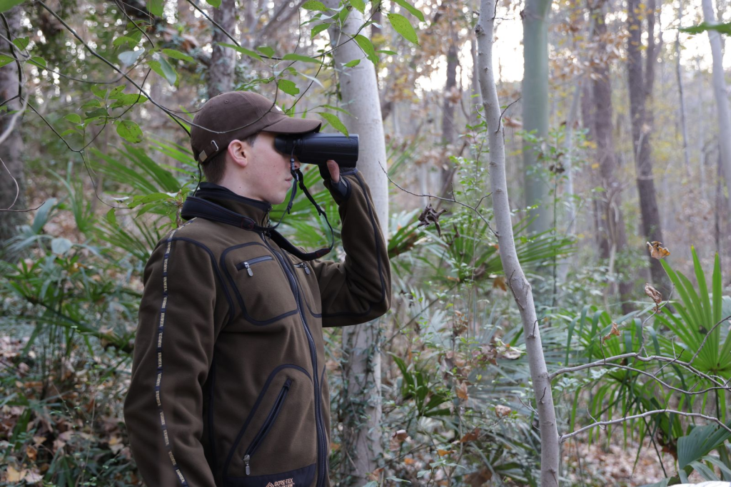 Person using binoculars to observe wildlife in a wooded forest area.