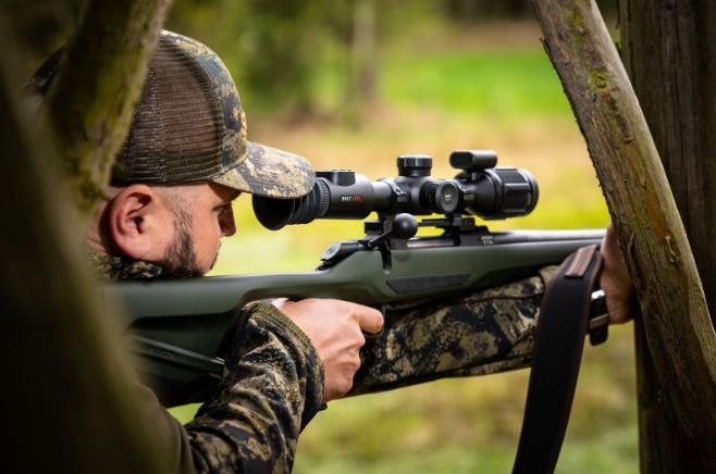 Cazador apuntando a través de la mira telescópica de un rifle mientras se prepara para ajustar la mira térmica en el campo.
