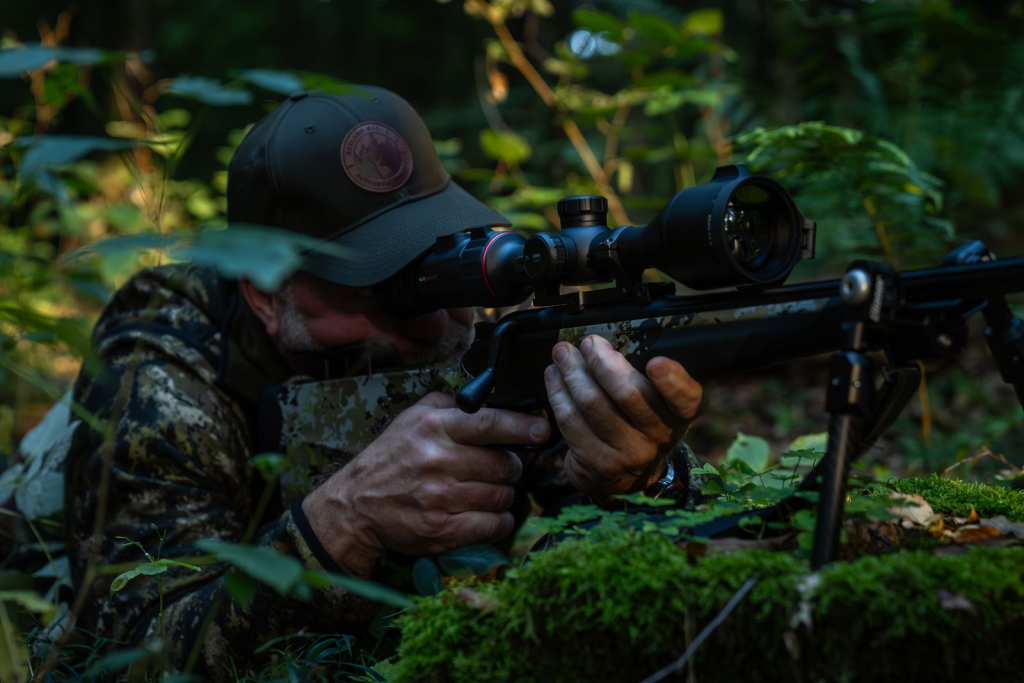 Chasseur visant avec un fusil équipé d'une lunette thermique en milieu forestier