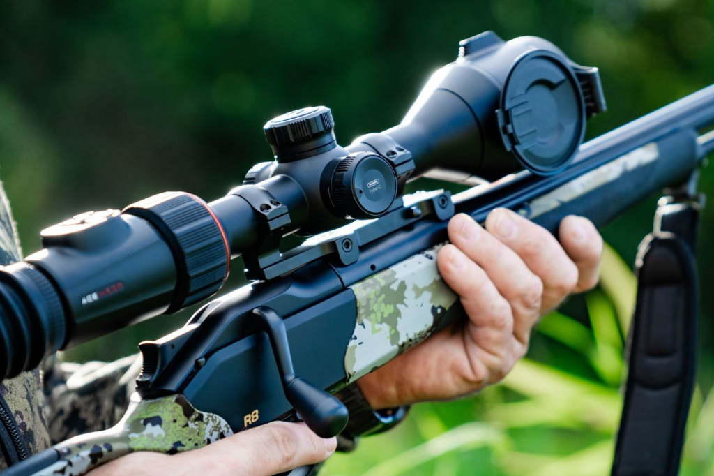 Close-up of a bolt-action rifle with a mounted riflescope held outdoors