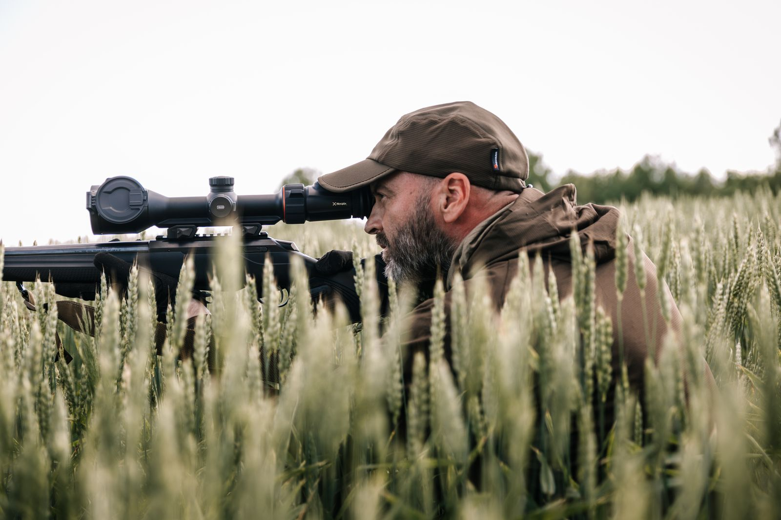 Hunter aiming a rifle with scope, focusing on a distant target.