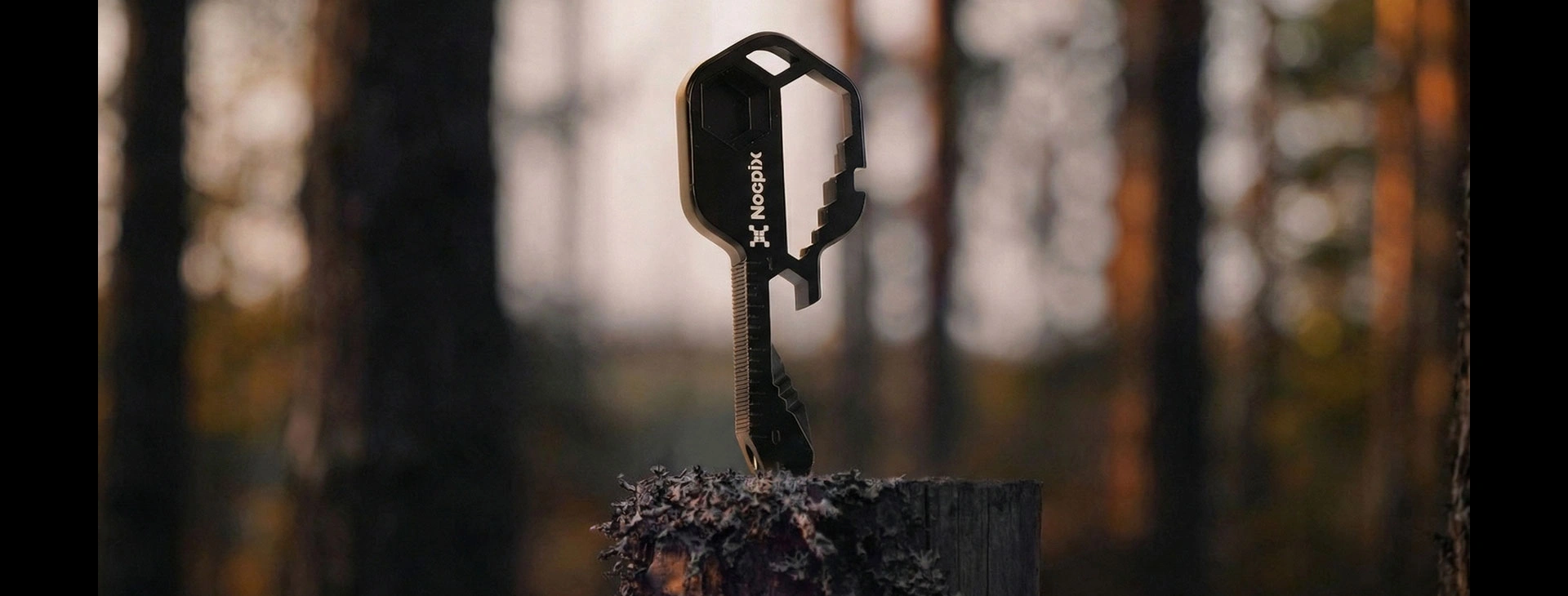 Nocpix nyckelformat multiverktyg stående på en mossig trädstubbe i en skog.