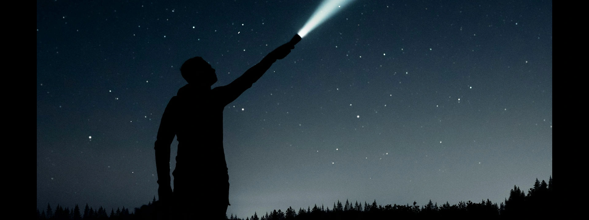 Person silhouette with flashlight under starry night sky.