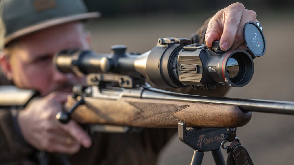 Hunter adjusting a thermal rifle scope mounted on a bolt-action rifle