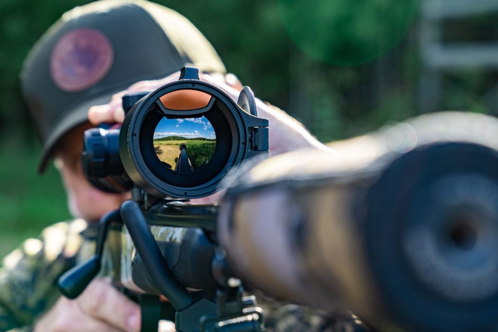Hunter looking through a rifle-mounted scope in an outdoor setting