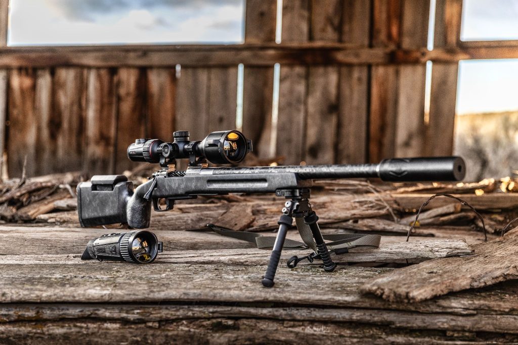 Rifle setup with mounted scope and thermal optic on a wooden platform