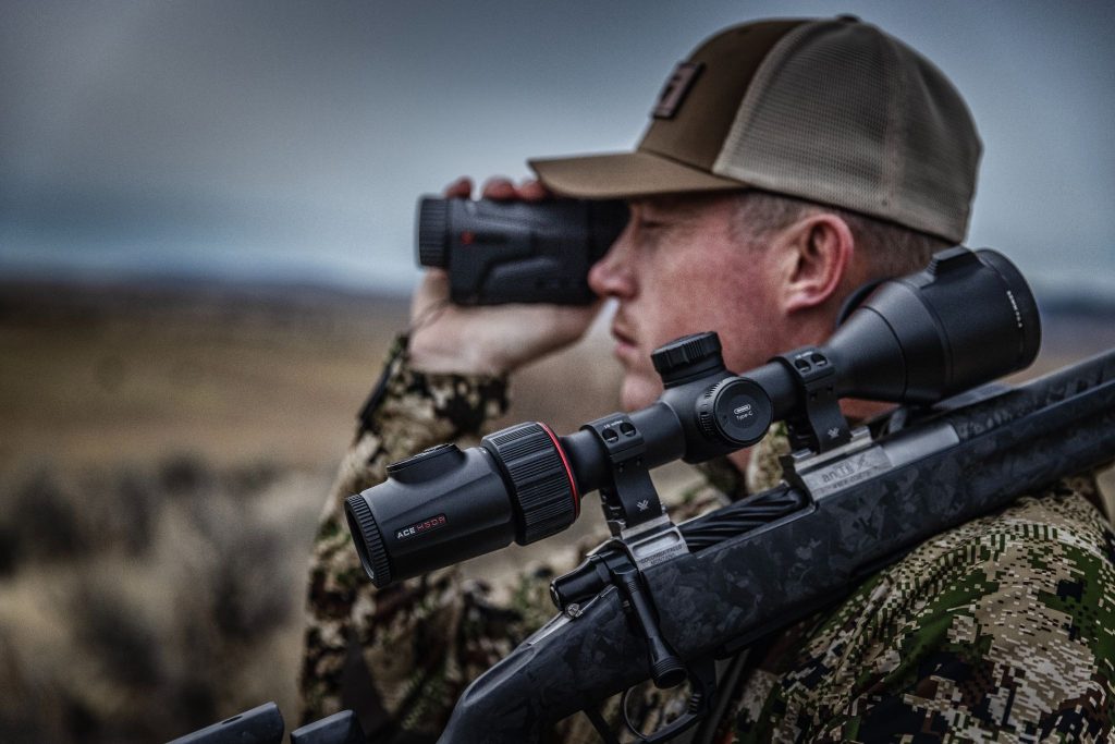 Hunter using a thermal scope and handheld thermal device in open terrain