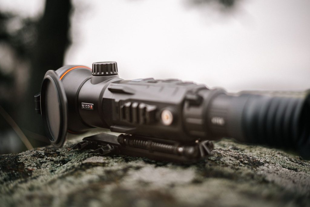 Close-up of a thermal scope mounted on a rifle in an outdoor setting