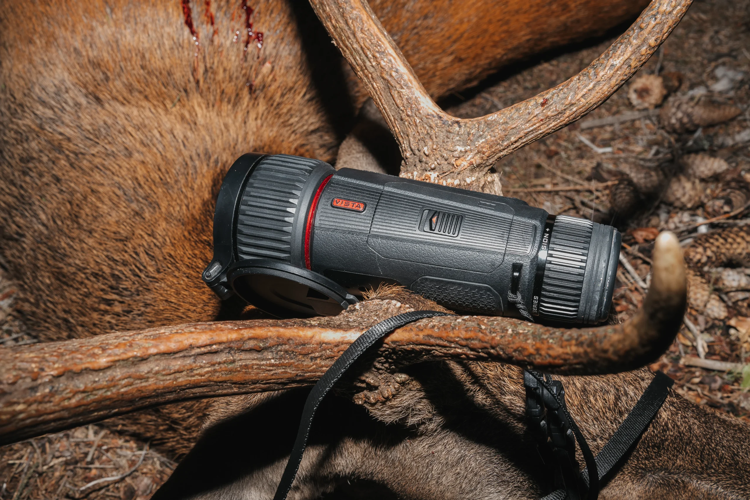 A handheld thermal monocular resting beside deer antlers after a woodland hunt.